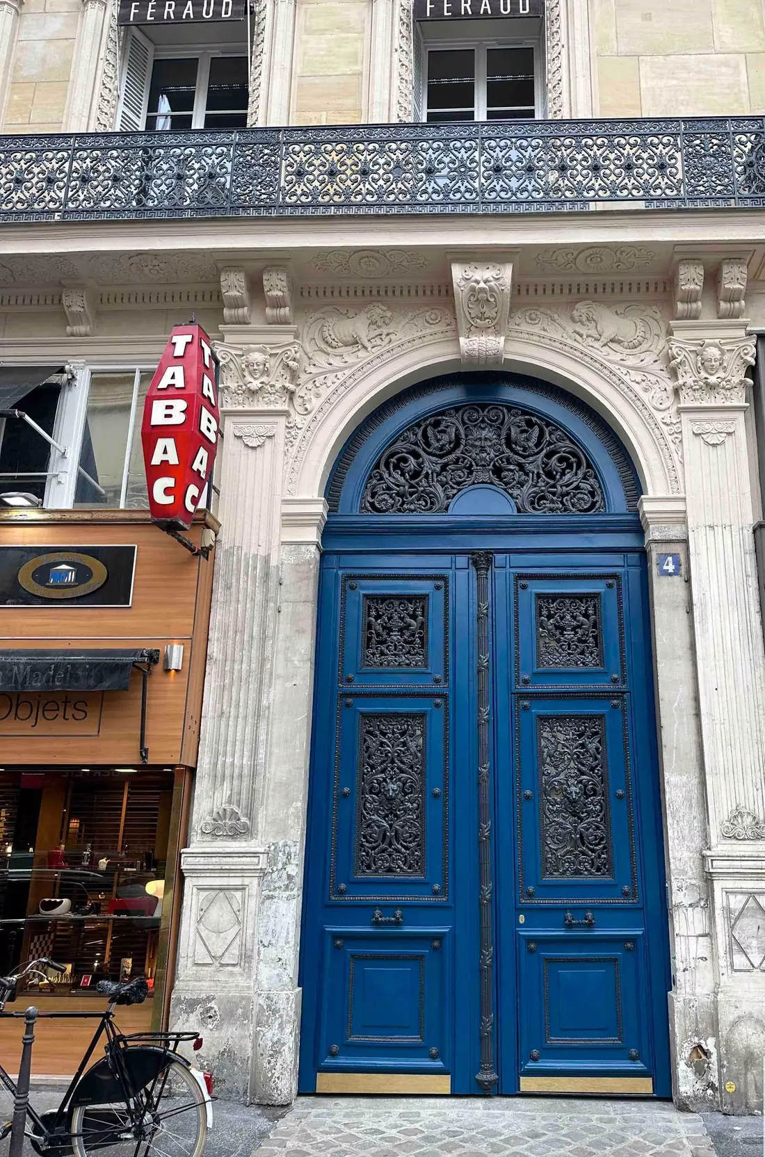 Porte cochère bleue à grilles sous une imposte ajourée, entre deux devantures