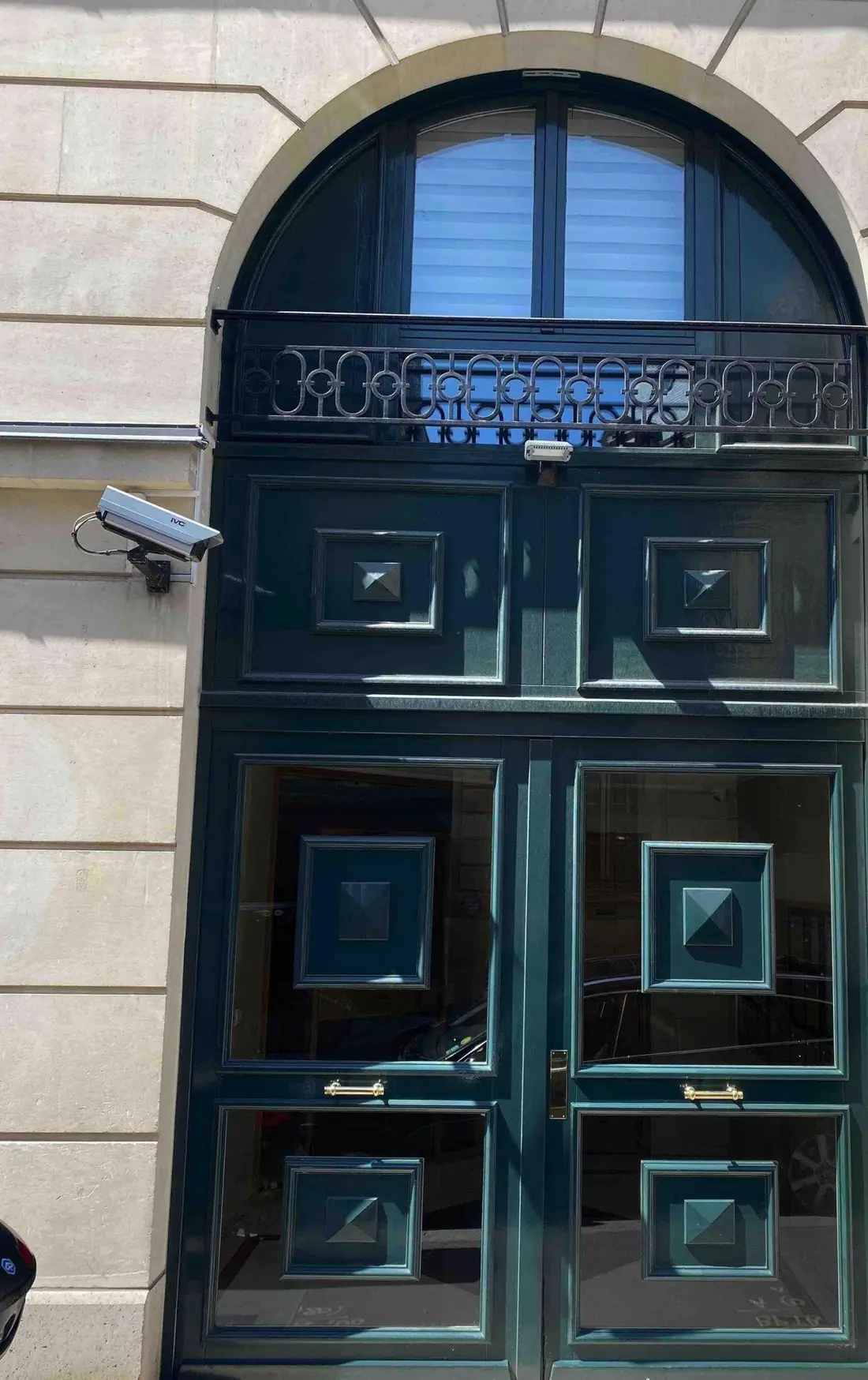 Porte cochère vert sombre à panneaux carrés, sous une baie cintrée vitrée