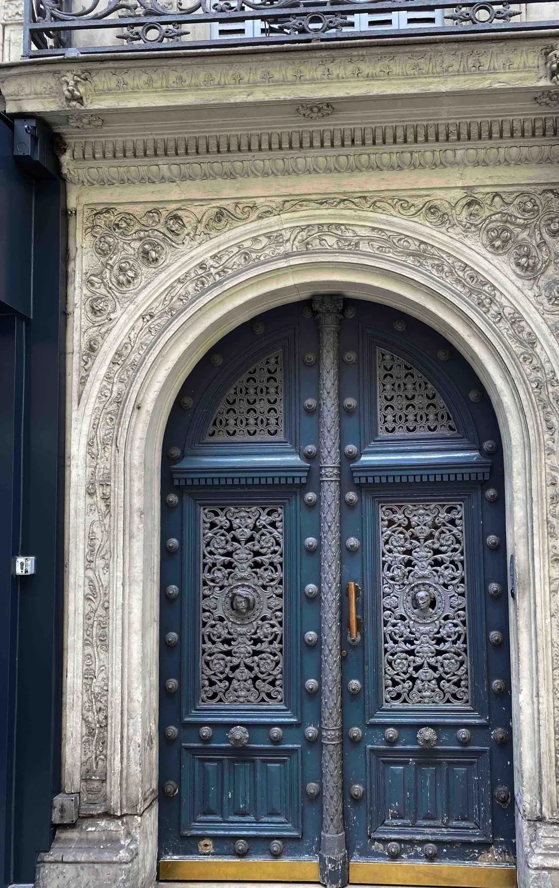 Porte cochère bleu sombre de style Empire à panneaux ajourés, dans un encadrement de pierre sculpté