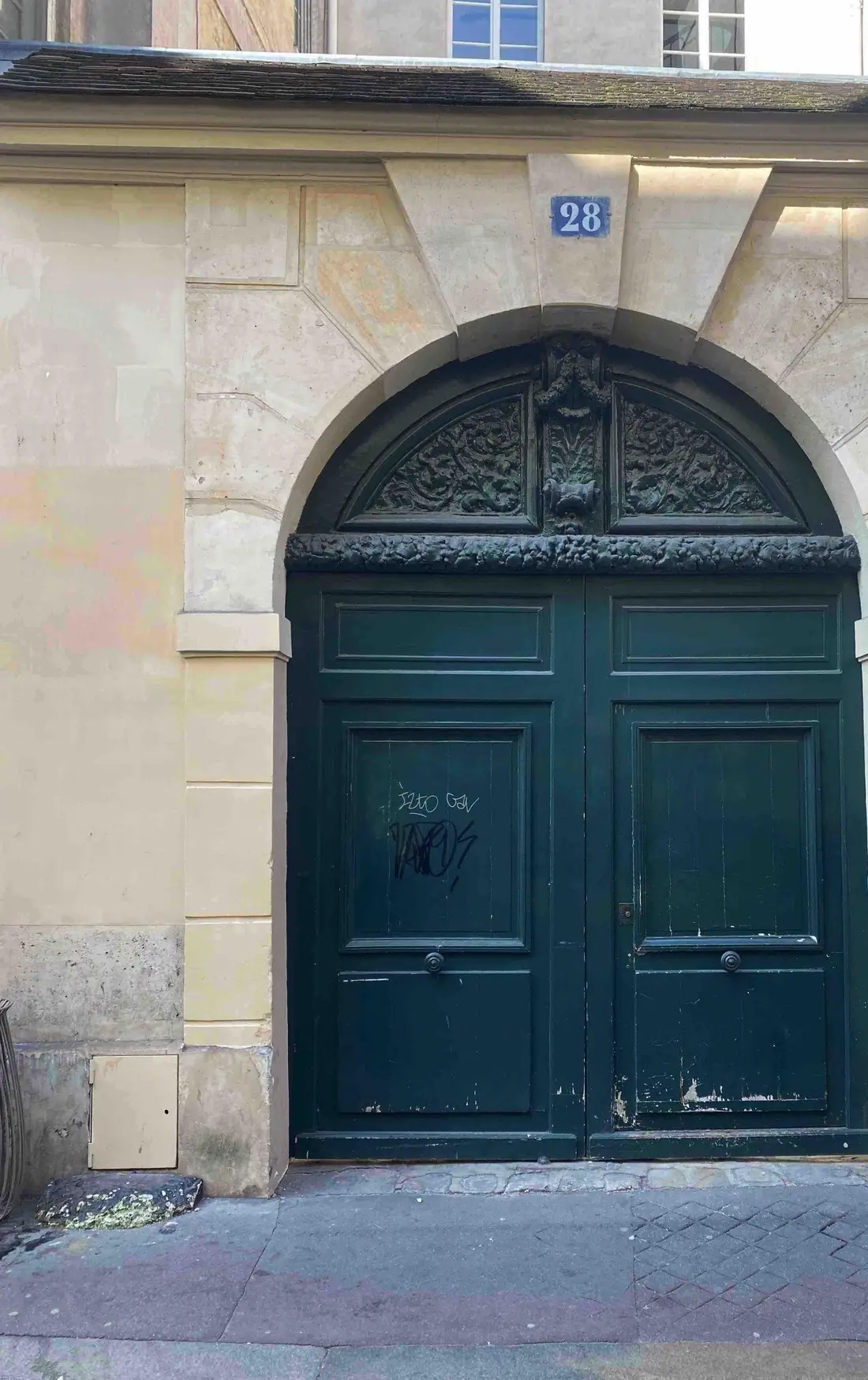 Porte cochère vert sombre cintrée, dans une façade de pierre