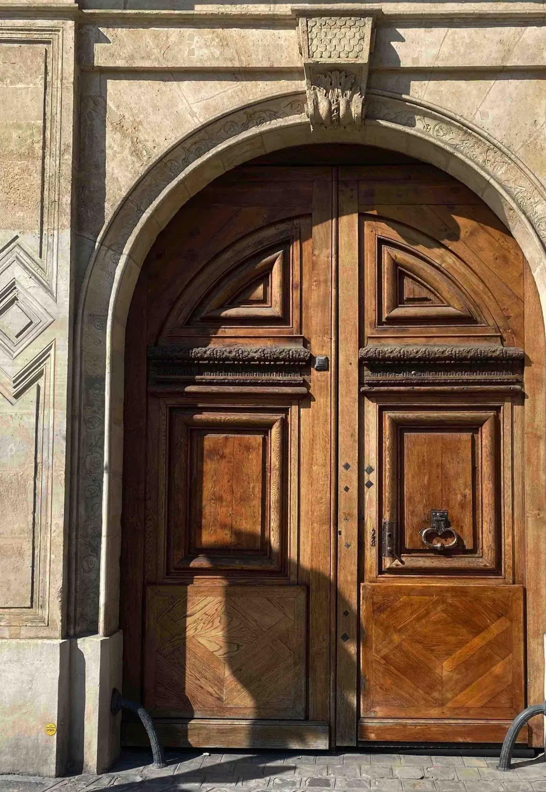 Porte cochère cintrée en chêne sombre à panneaux ornés, sous une grande arcade