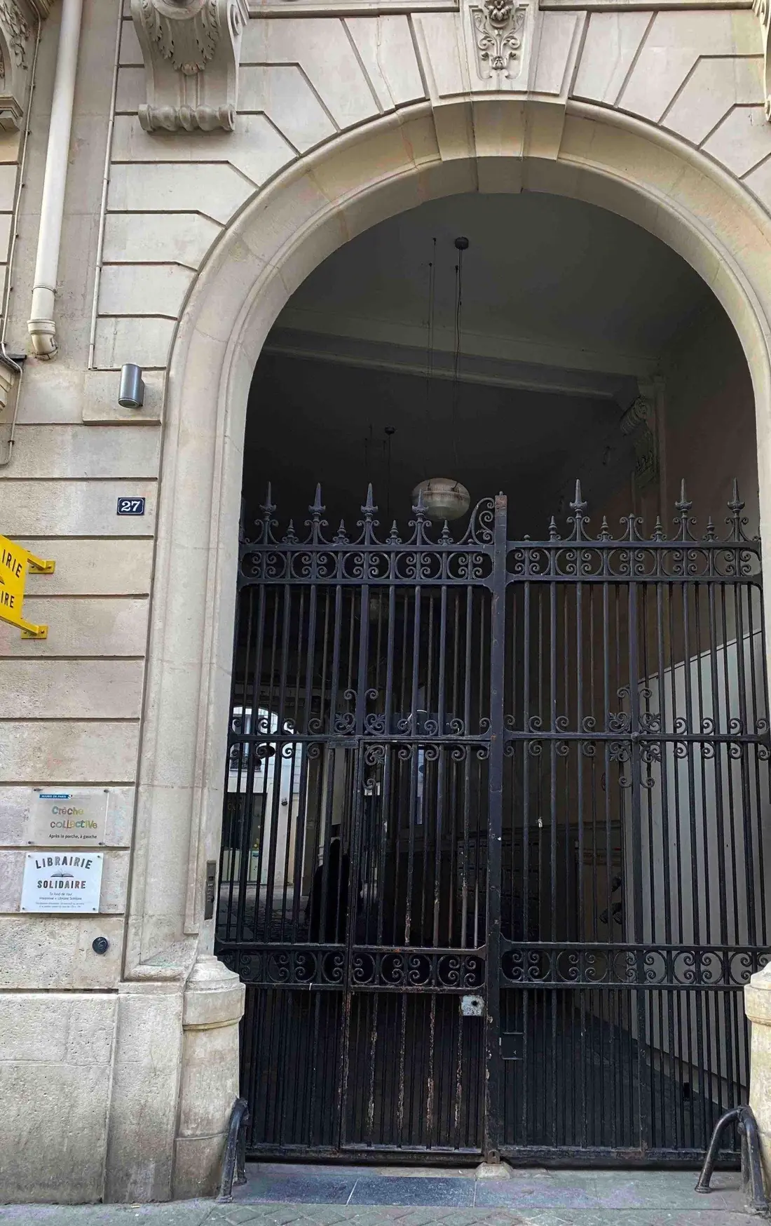 Porte cintrée en grille d’acier laissant voir le porche, façade claire