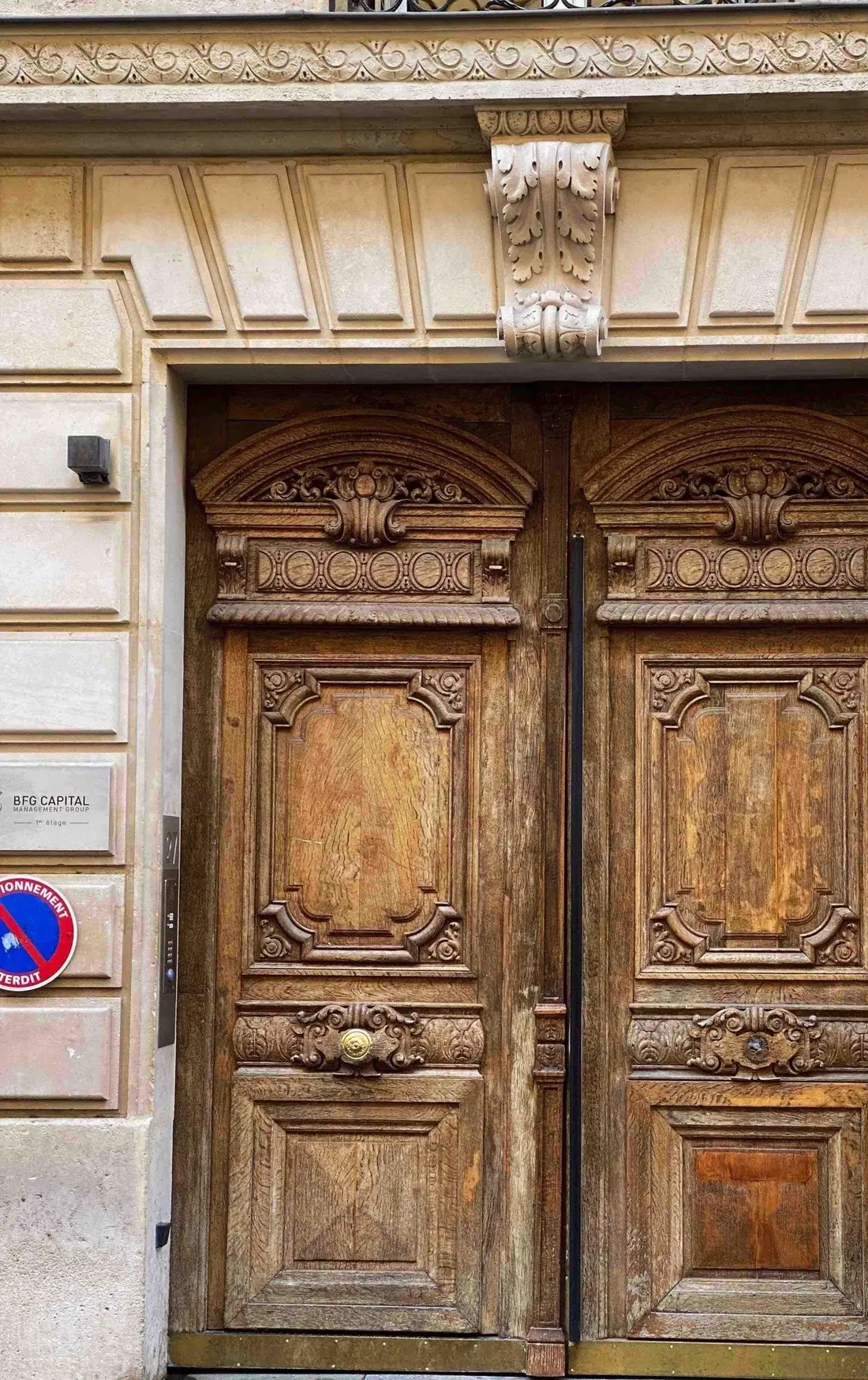 Porte cochère en bois naturel à panneaux sculptés, encadrée de pierre