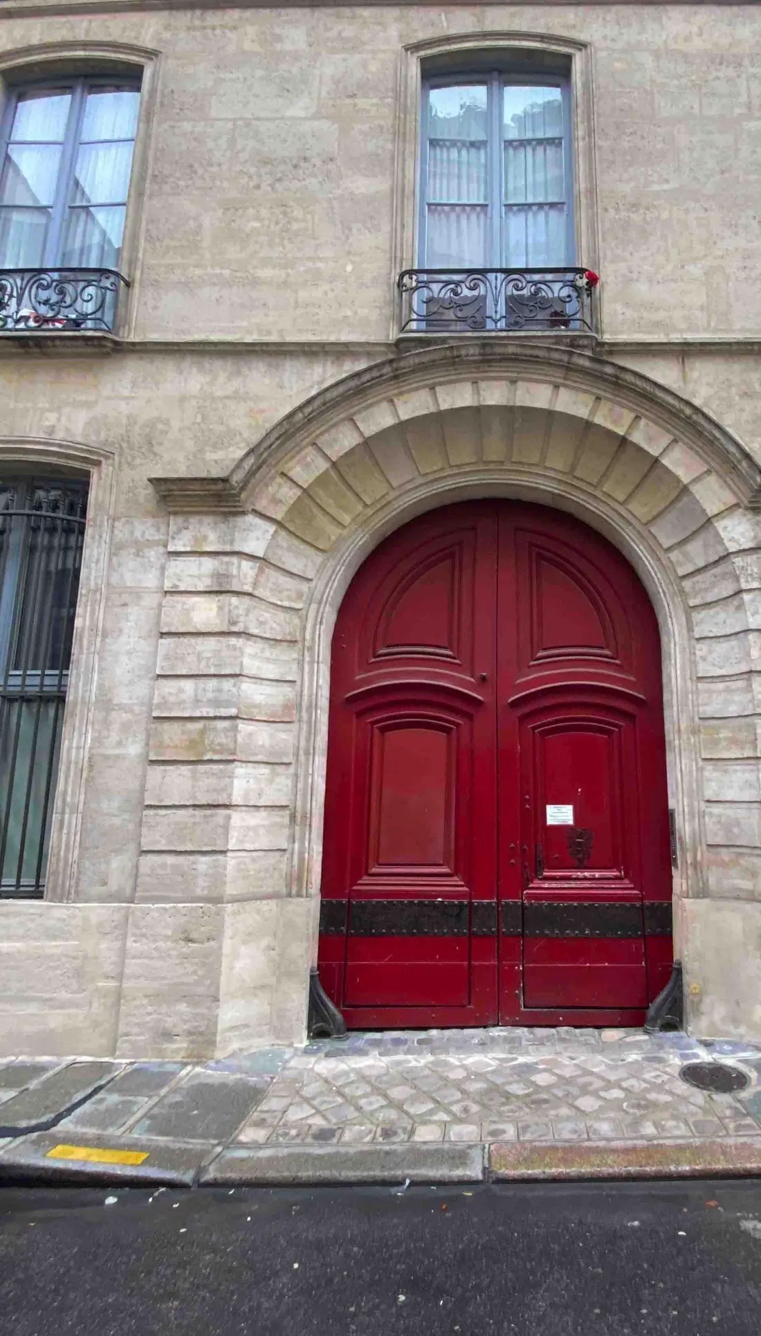 Porte cochère rouge Louis XIII sous un arc de pierre, façade du Marais
