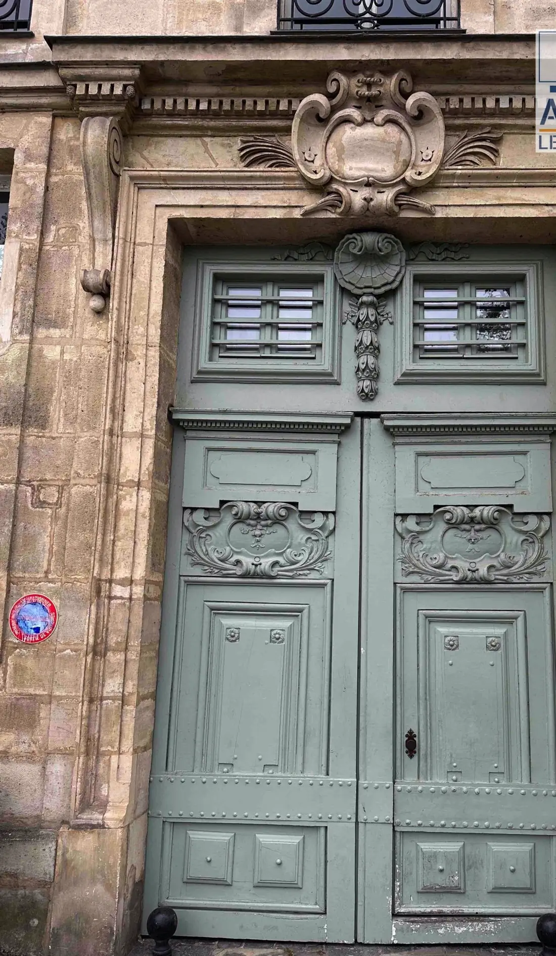 Porte cochère gris-vert à panneaux sculptés, sous un cartouche de pierre