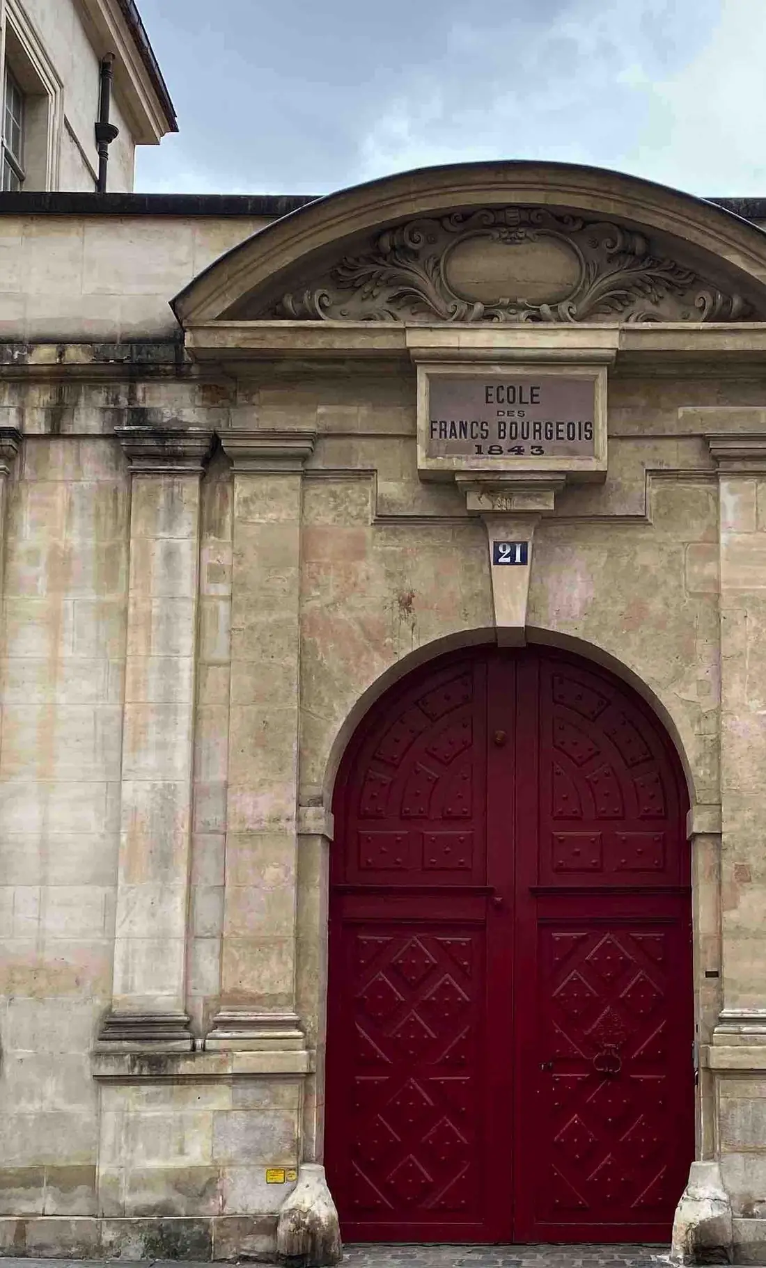 Porte cochère rouge Louis XIII cintrée, sous une façade de pierre