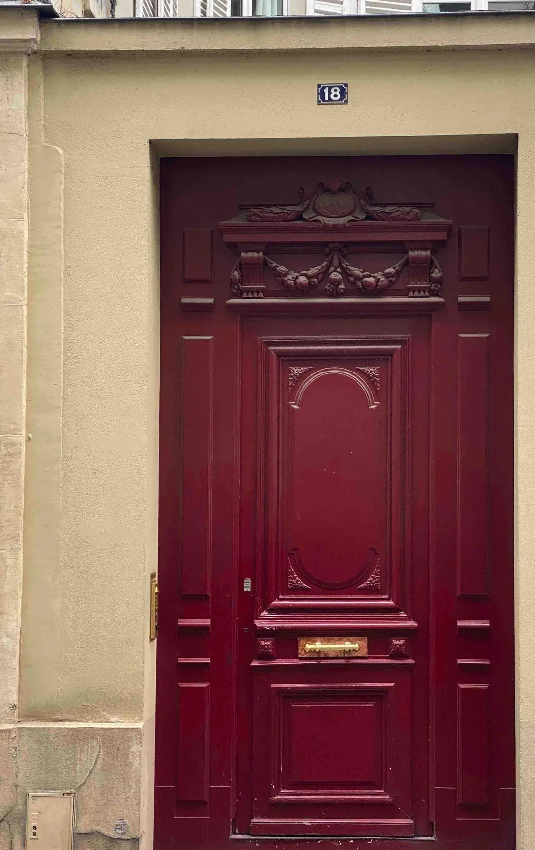 Porte piétonne rouge à panneaux moulurés, dans un encadrement de pierre