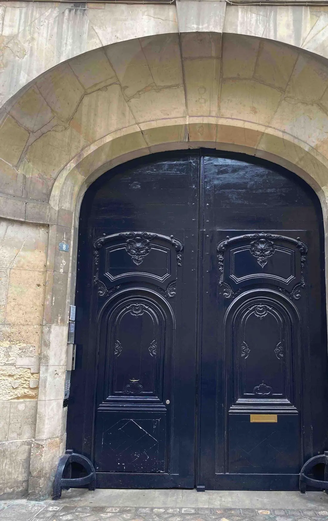 Porte cochère Louis XIII bleu nuit à panneaux sculptés, sous un arc de pierre