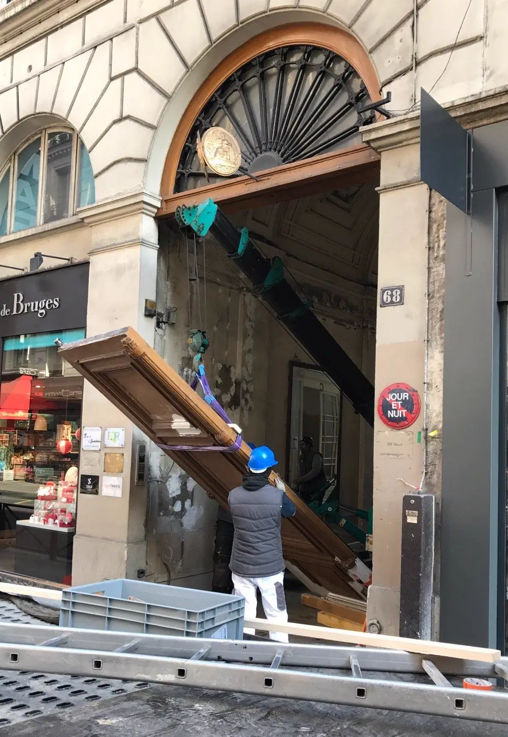 Vantail de porte cochère monumentale soulevé au palan sous une imposte en éventail, compagnon au pied