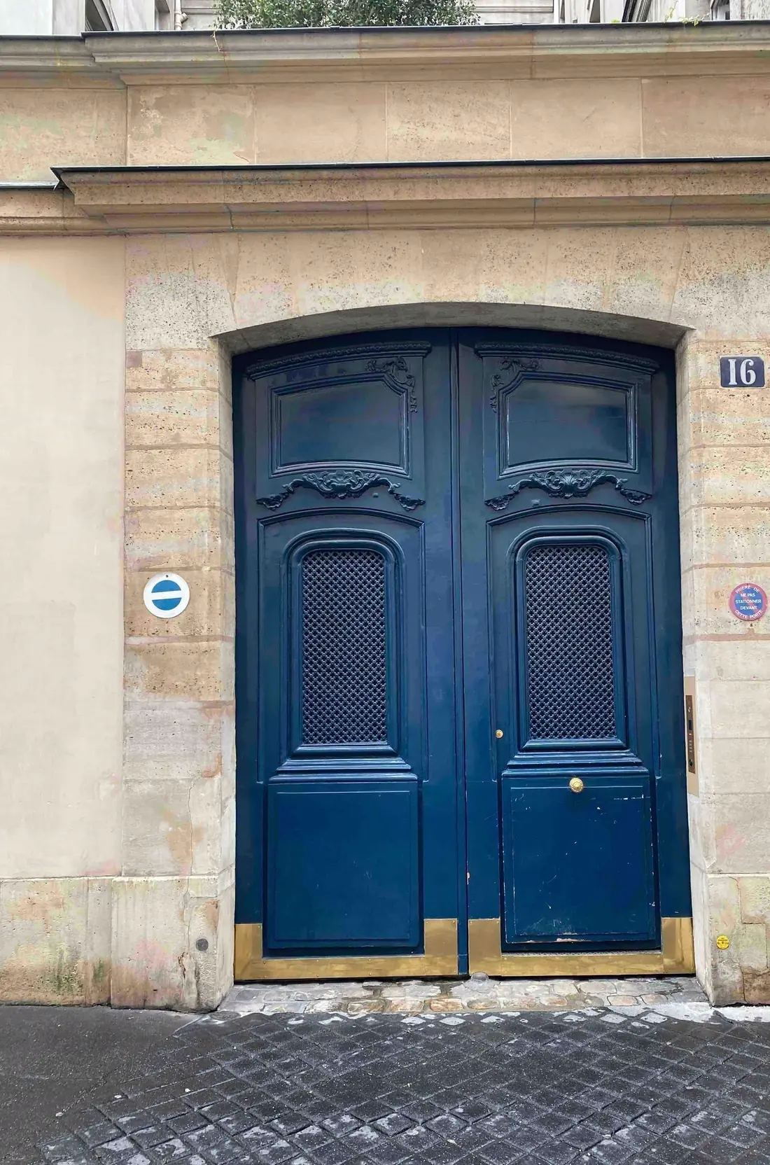 Porte cochère bleue dont le pied des vantaux est entaillé, chantier ouvert sur bâche