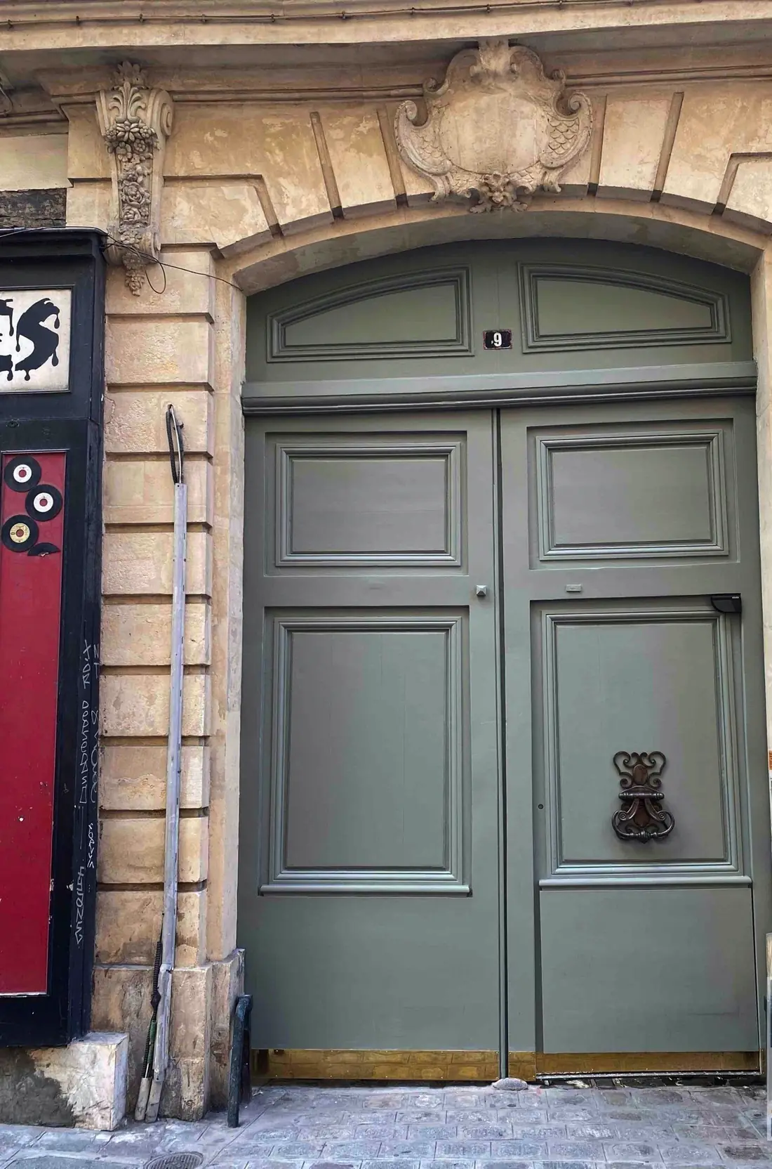 Porte cochère vert-de-gris à heurtoir, sous un encadrement de pierre sculpté