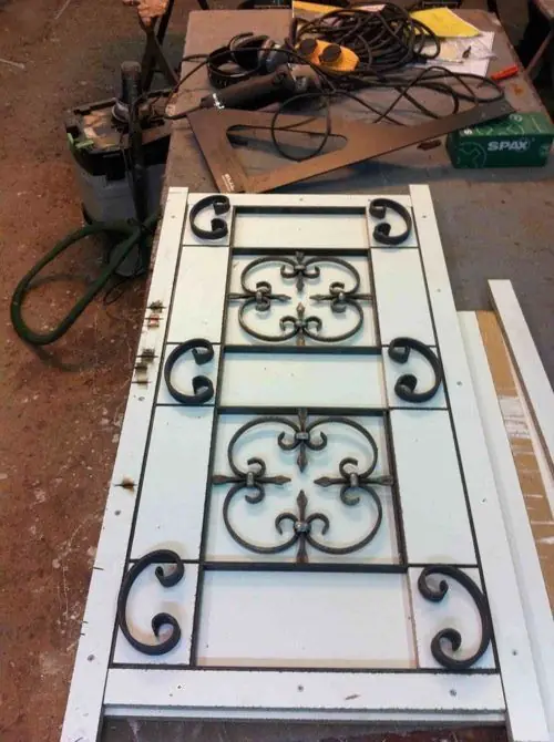 Grille en fer forgé à volutes posée à plat sur une porte vitrée, à l’atelier