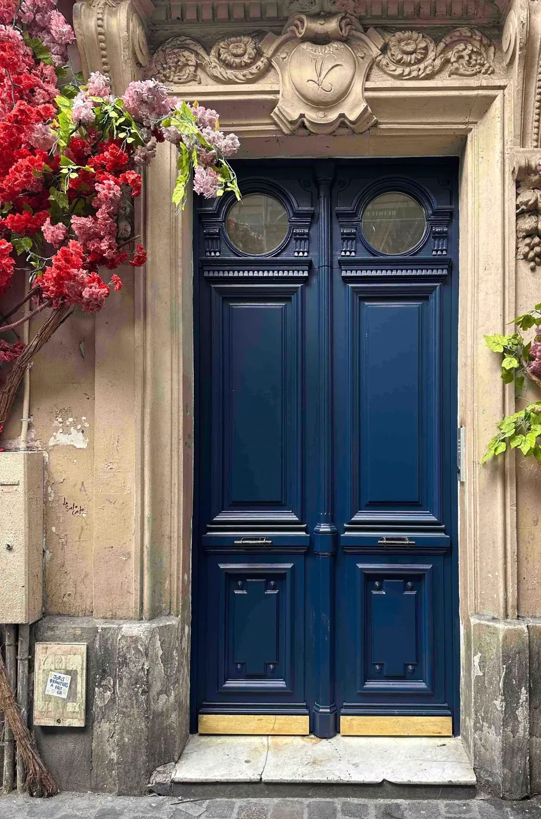 Porte cochère bleu nuit dans un encadrement de pierre sculpté, fleurs en façade