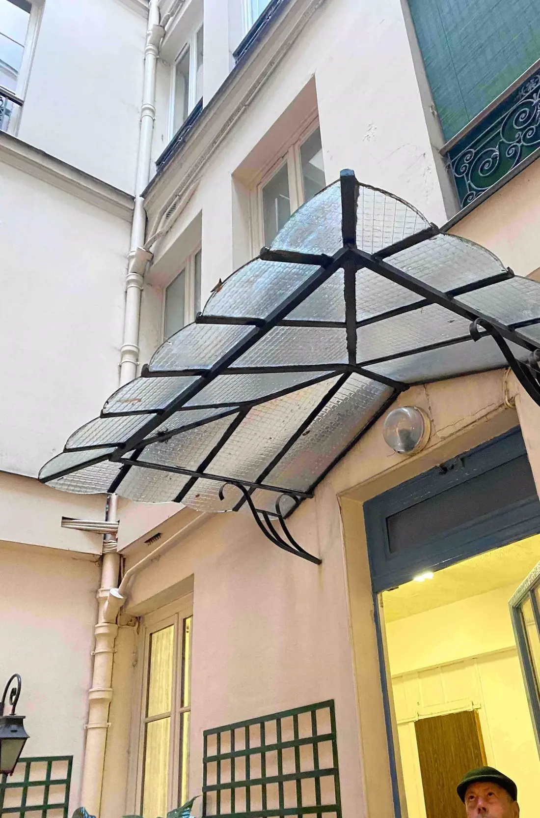 Marquise en acier et verre déployée en éventail au-dessus d’une porte de cour