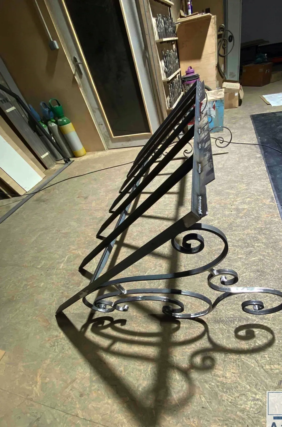 Marquise en fer forgé à volutes posée sur le sol de l’atelier, son ombre portée au sol