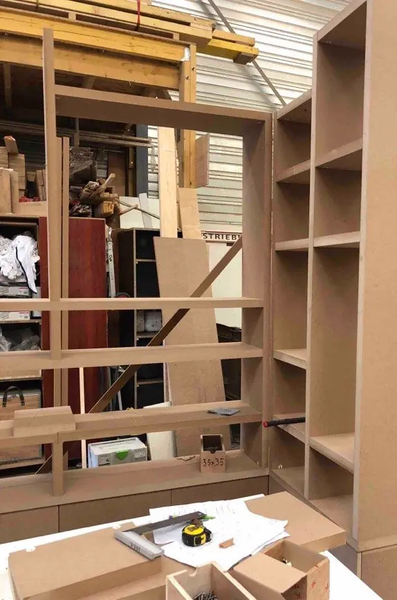 Agencement en médium épais monté à blanc dans l’atelier, étagères et caissons, outillage sur l’établi