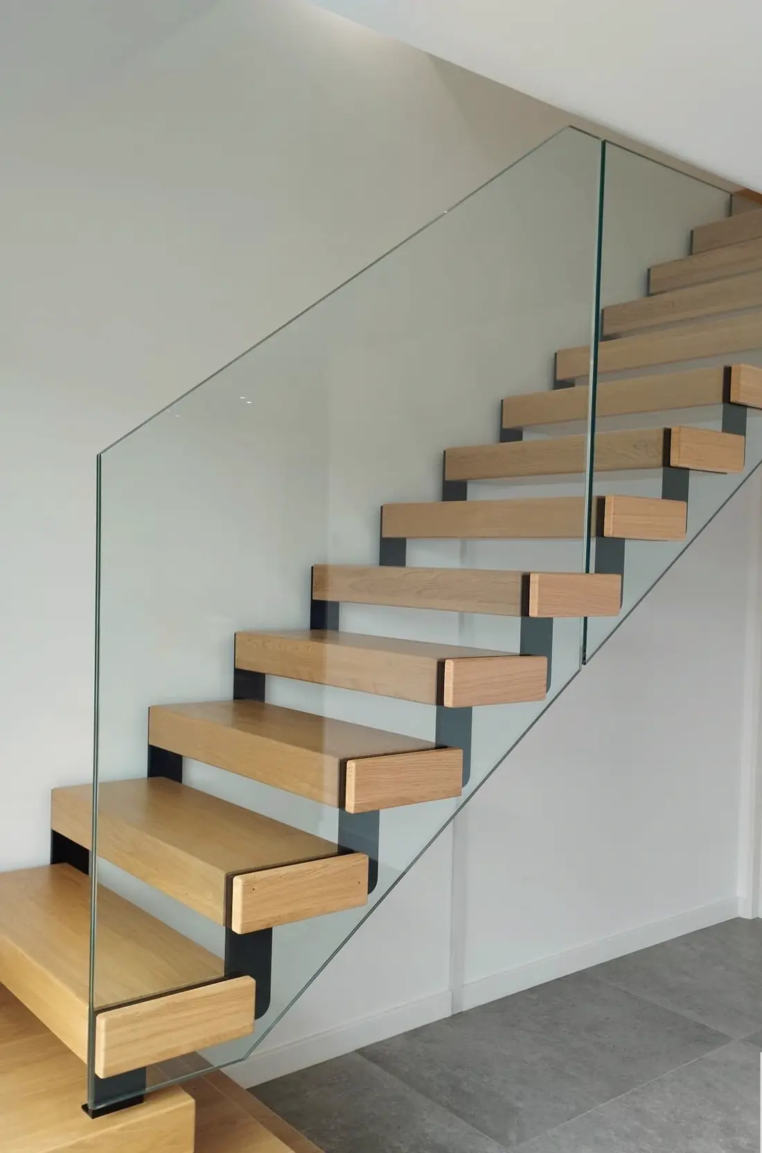 Escalier droit à marches de bois clair sur limon acier noir, garde-corps en verre