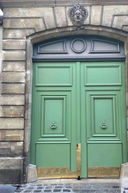 Porte cochère neuve peinte en vert, deux vantaux à panneaux et heurtoirs, sous un mascaron