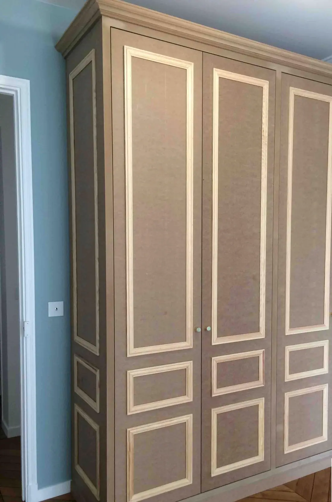 Placard à trois portes ornées de moulures en applique, dans une chambre à parquet point de Hongrie