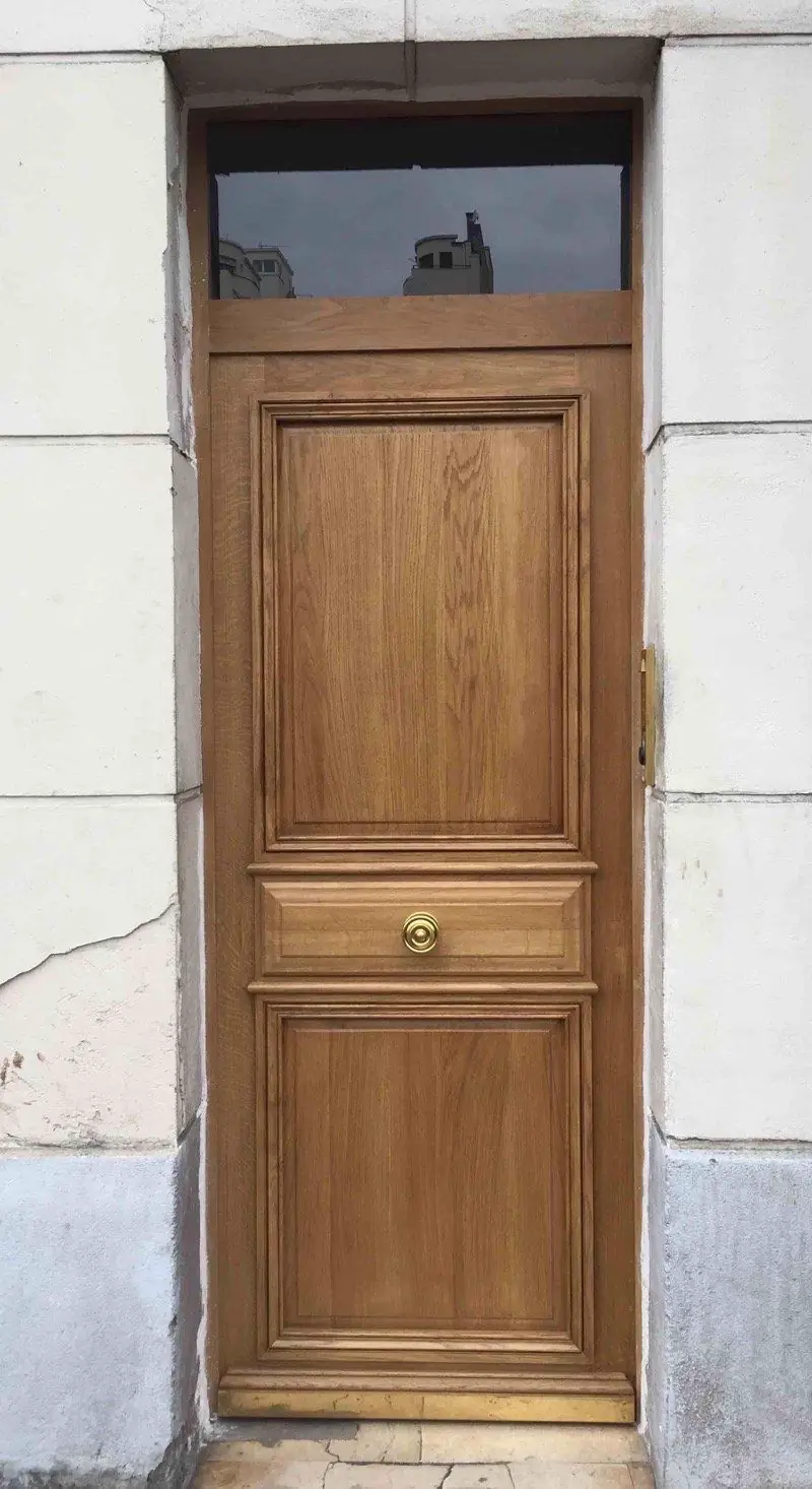 Porte pleine en chêne verni à panneaux, surmontée d’une imposte vitrée