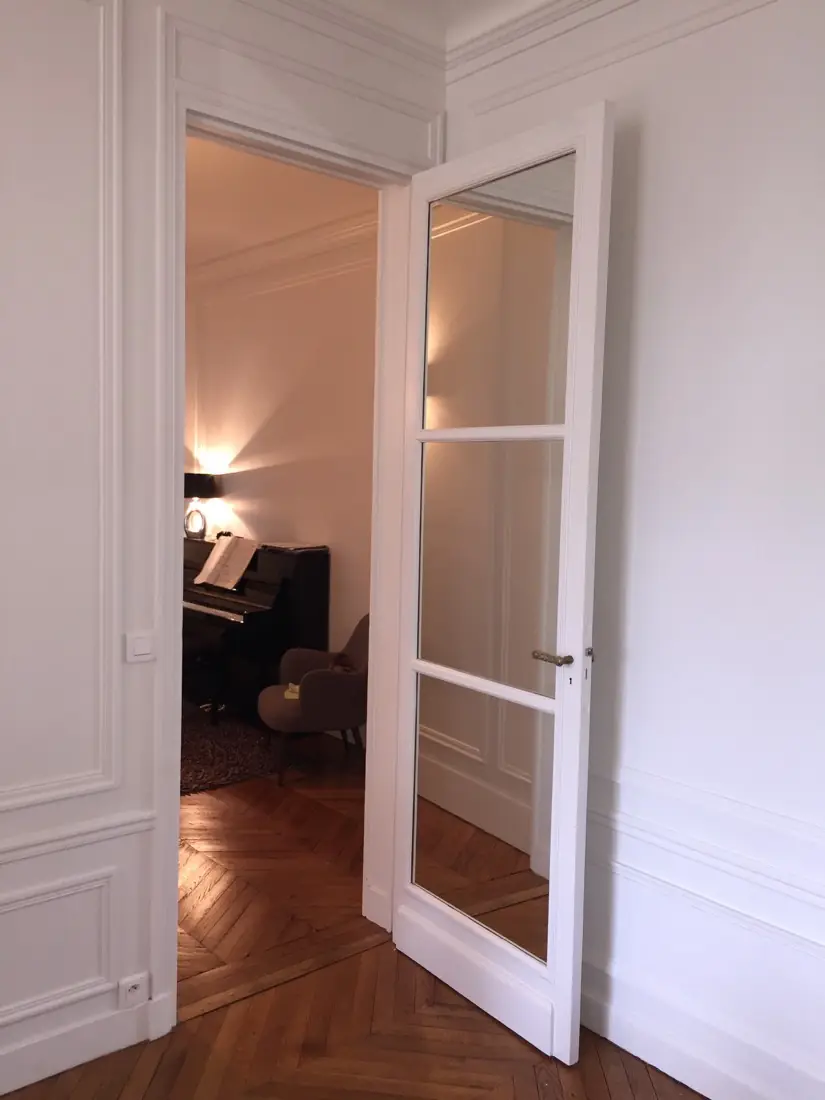 Porte intérieure vitrée blanche à petits bois, ouverte sur un parquet à bâtons rompus