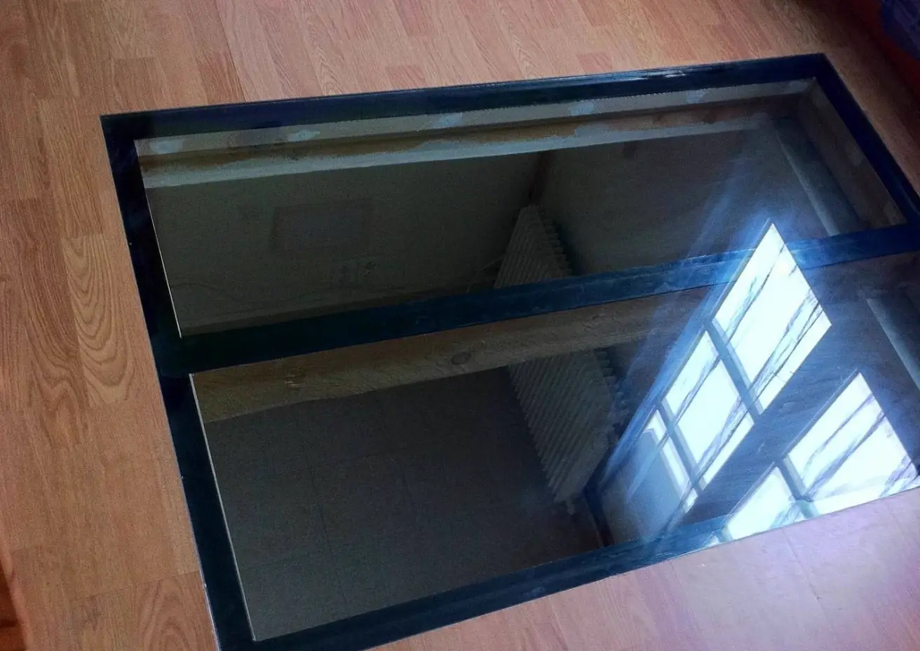 Dalle de verre encastrée dans un parquet, laissant voir la fenêtre de l’étage inférieur