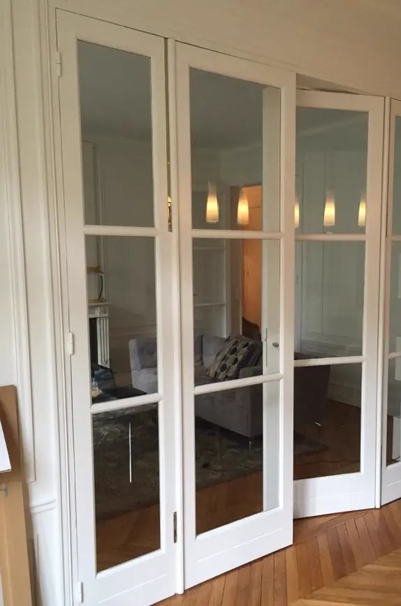 Porte intérieure vitrée à quatre vantaux blancs, petits bois et moulures, dans un appartement haussmannien