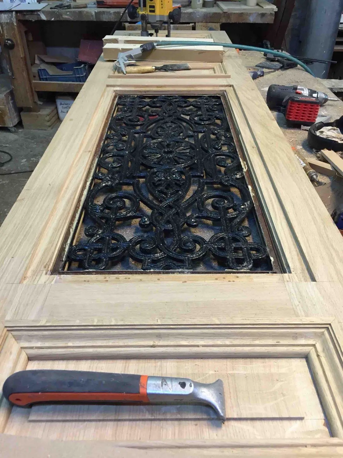 Vantail en chêne clair posé sur l’établi, autour d’une grille ancienne en fer forgé remployée