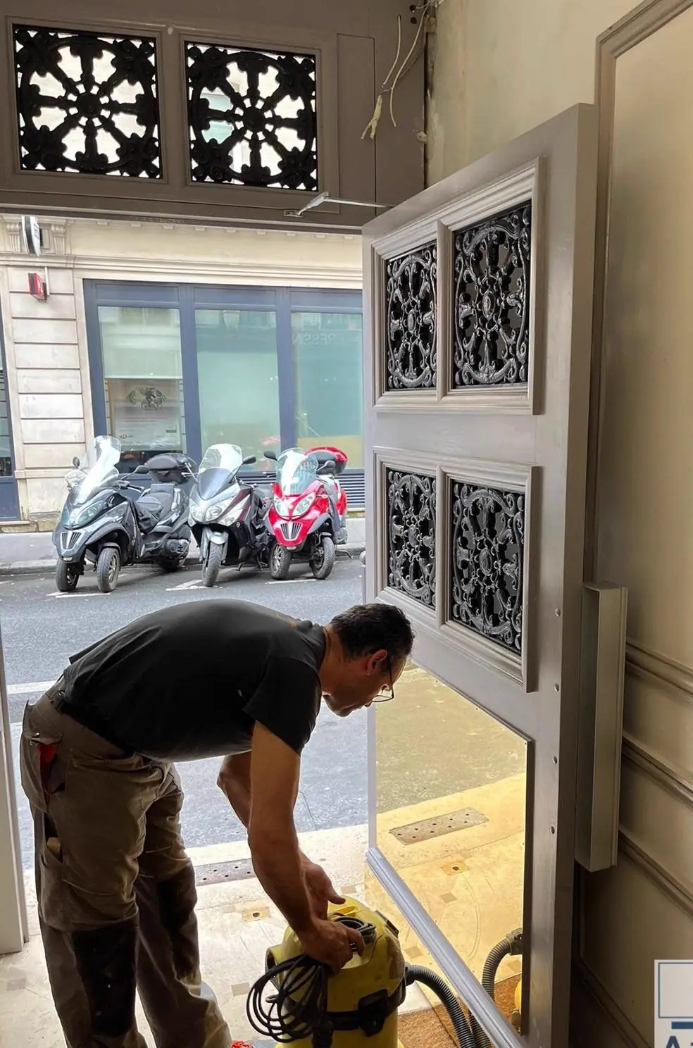 Compagnon penché, aspirateur en main, au pied d’une porte d’immeuble en cours de repose