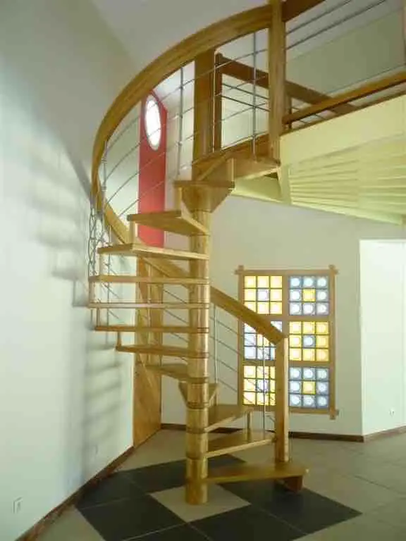 Escalier hélicoïdal en bois à balustres inox, devant une fenêtre à petits carreaux