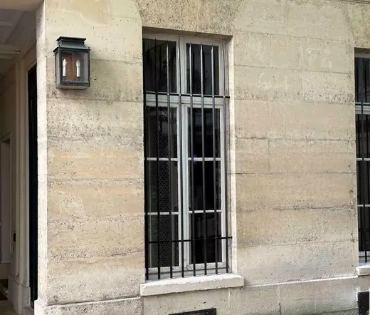 Deux fenêtres équipées de grilles de défense sur une façade en pierre de taille, lanterne murale