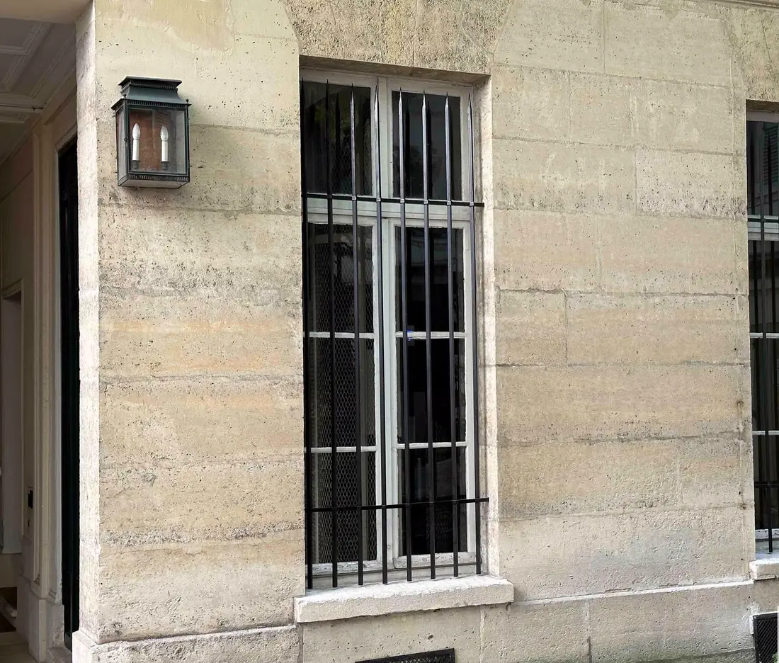 Deux fenêtres équipées de grilles de défense sur une façade en pierre de taille, lanterne murale